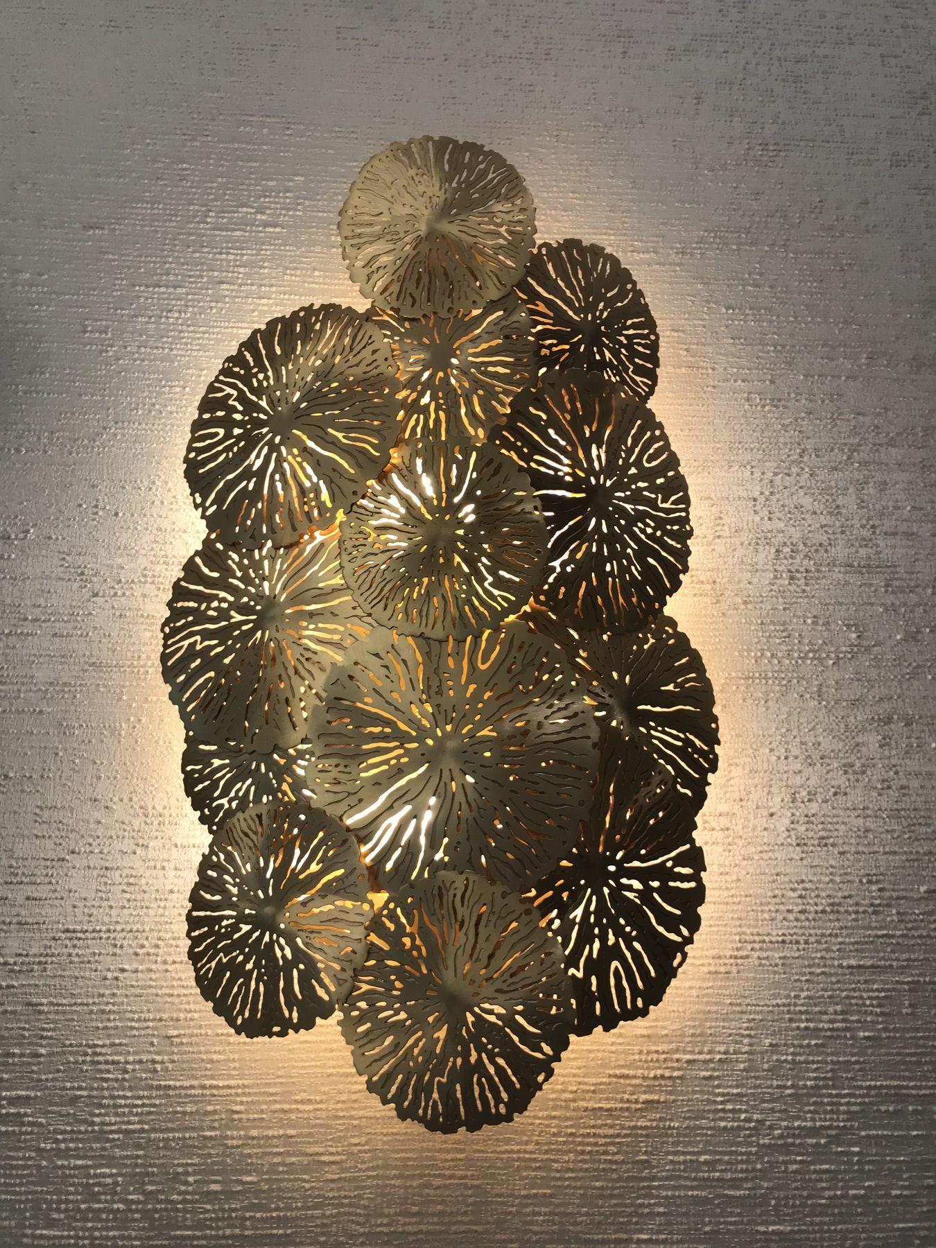 Pierced brass wall light glowing against textured plaster