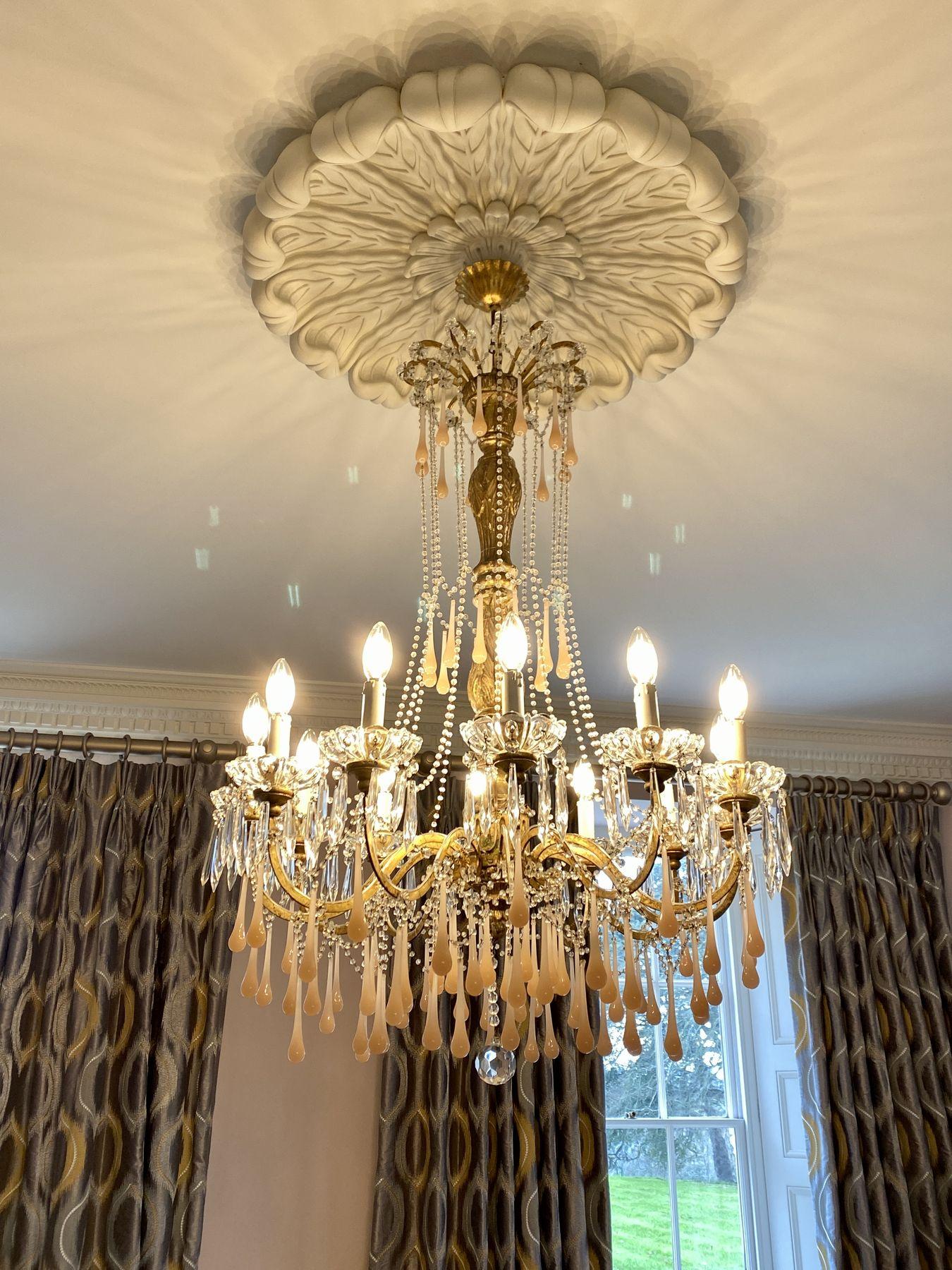 Gilt chandelier with pink glass drops, lit in a drawing room