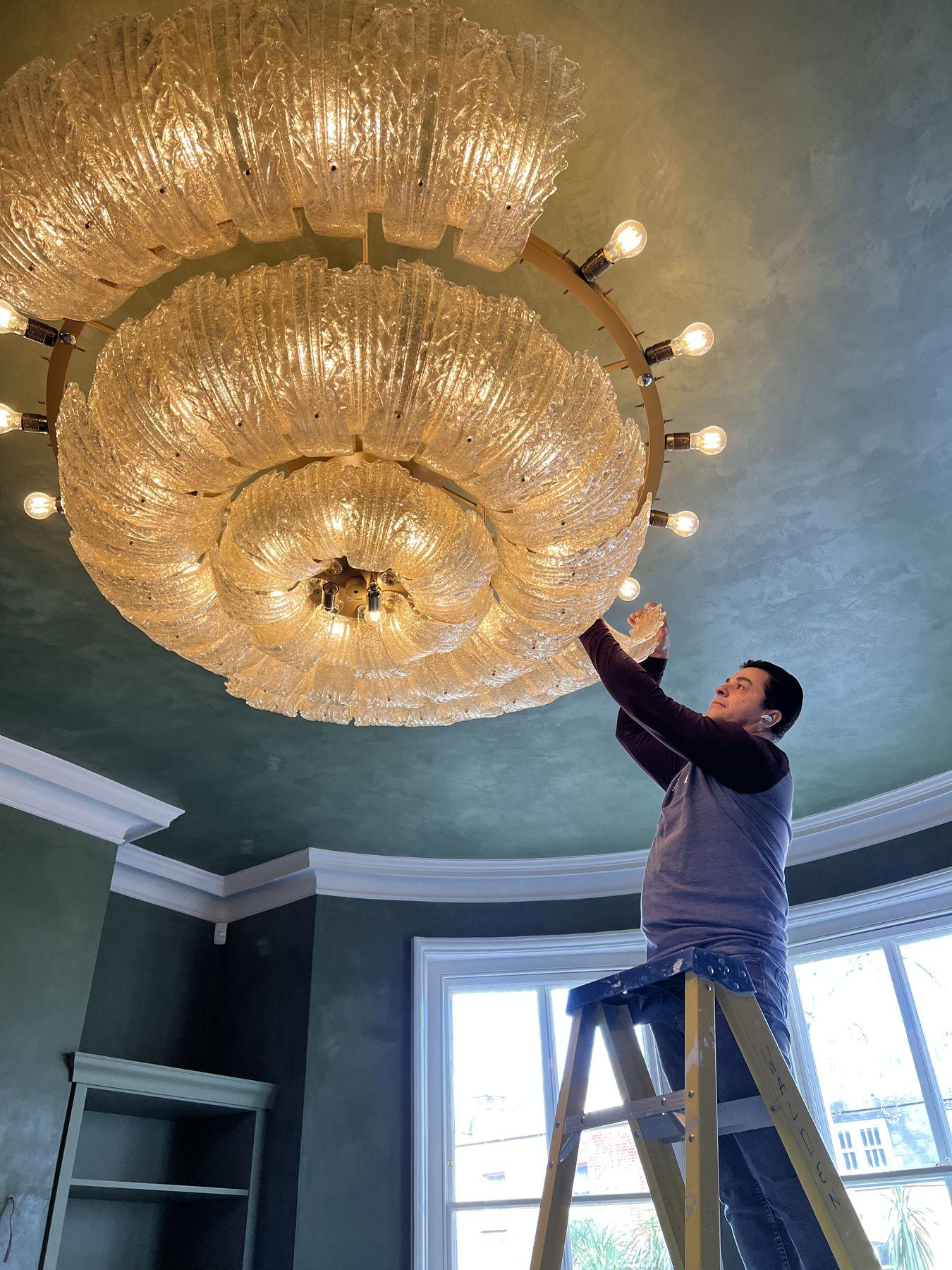 Marcos Lira Brandão on a ladder fitting a Murano glass chandelier